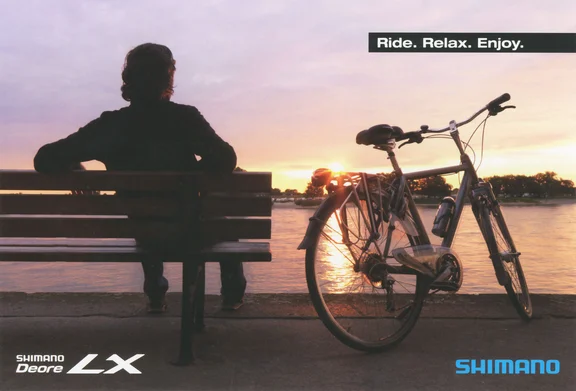 Person auf einer Bank an einem See bei Sonnenuntergang, rechts daneben ein Fahrrad