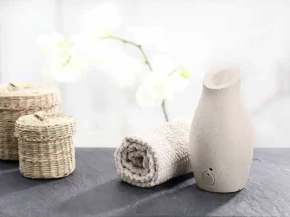 Steinvase auf Schiefer, eingerolltes Handtuch und Körbe links, weiße Orchidee im Hintergrund