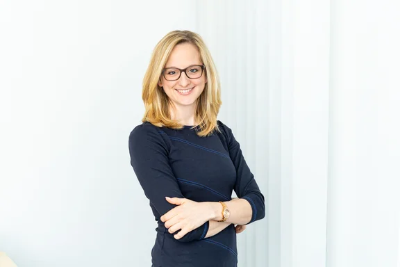 Portrait von einer Frau mit blonden langen Haaren mit Brille in einem dunkelblauem Oberteil