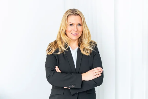 Portrait von einer Frau mit langen blonden Haaren in einem schwarzen Anzug und weißem Oberteil