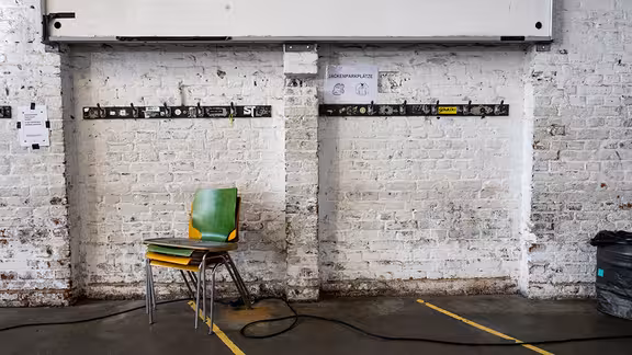 Stühle vor einer gemauerten weißen Wand mit Jackenhacken