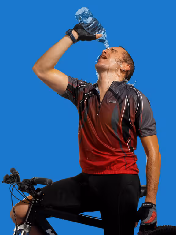 Mann in Sportkleidung auf einem Fahrrad übergießt sich mit Wasser aus einer Flasche, Blick von schräg unten