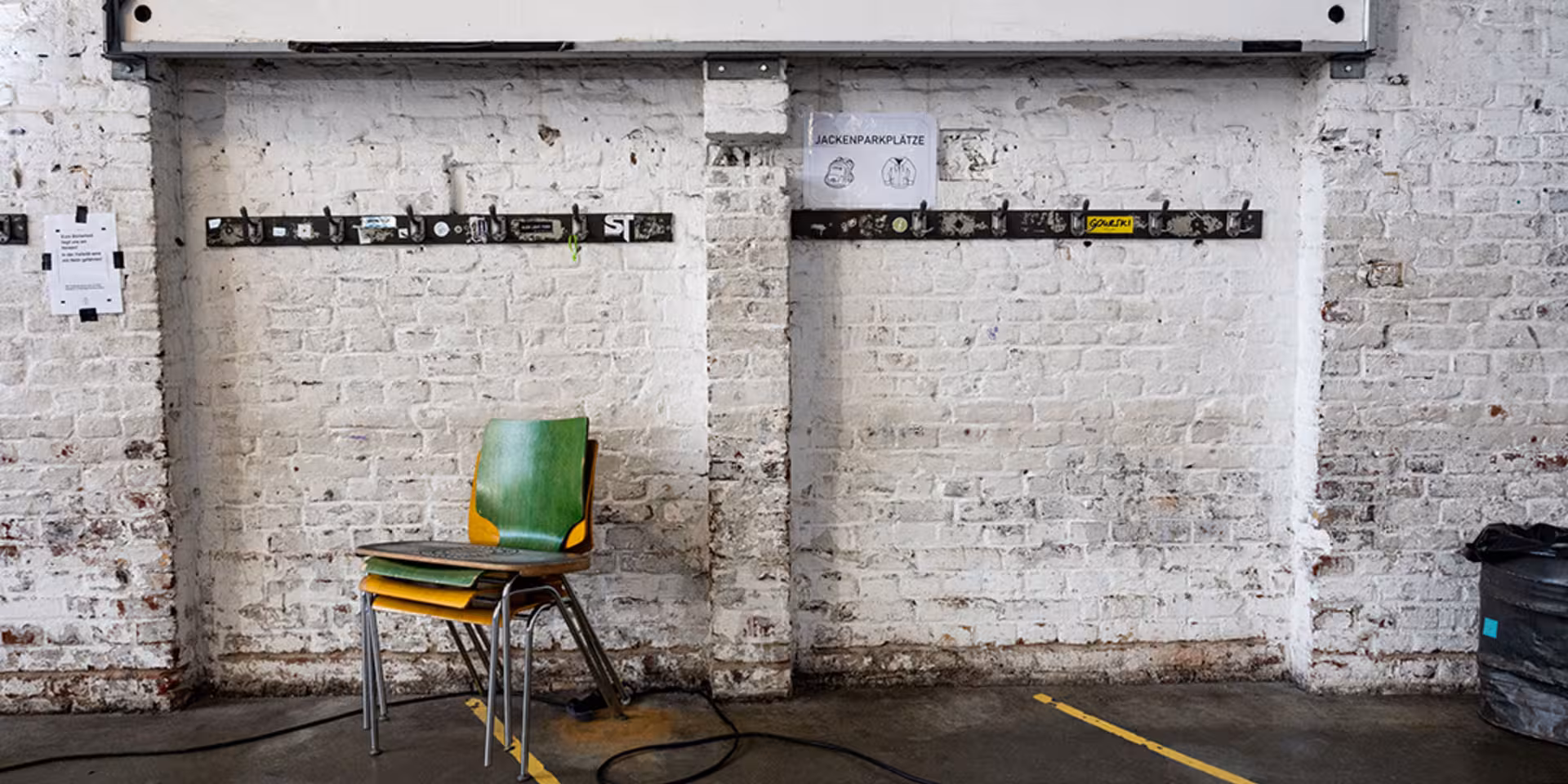 Stühle vor einer gemauerten weißen Wand mit Jackenhacken